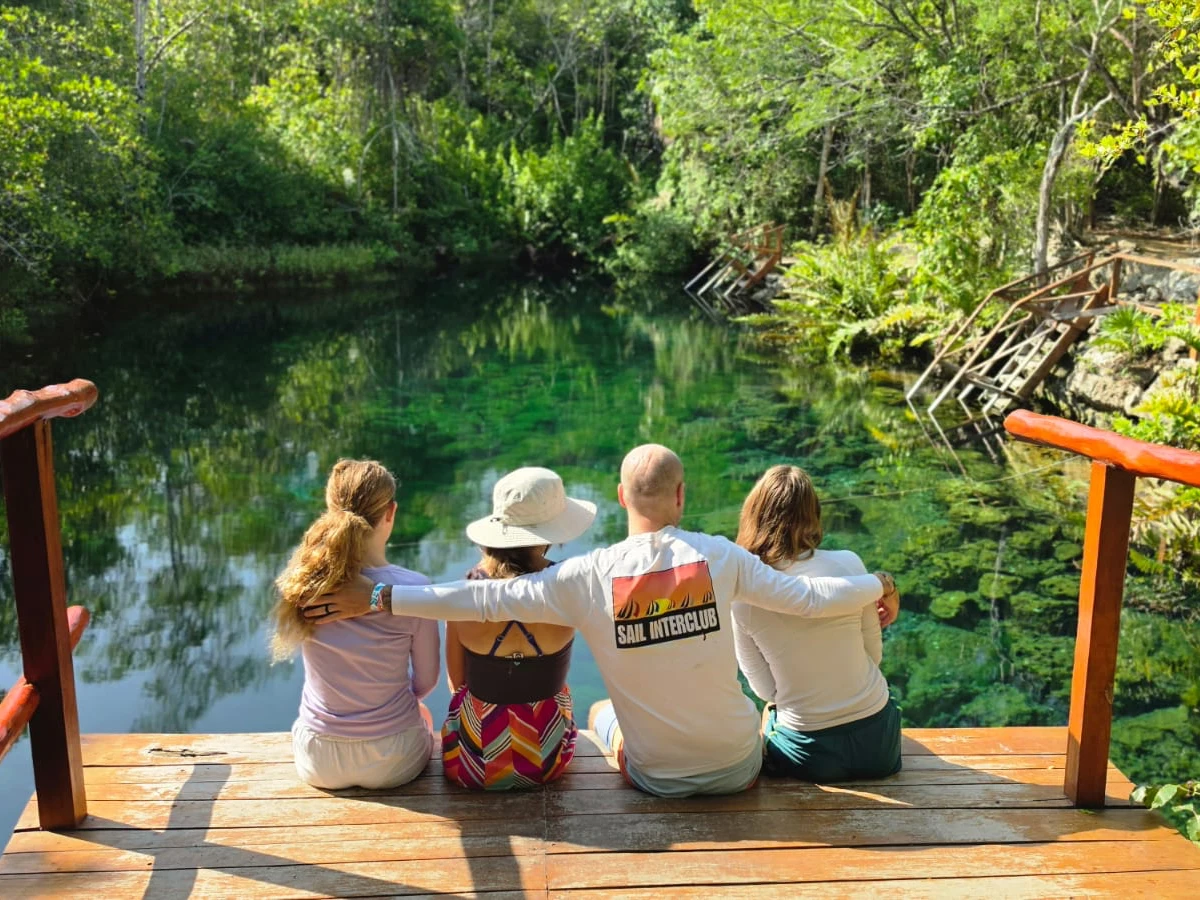 A family sitting together on a wooden platform overlooking a cenote.