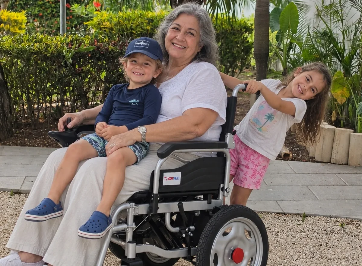 Older woman seated in a wheelchair with two smiling children nearby